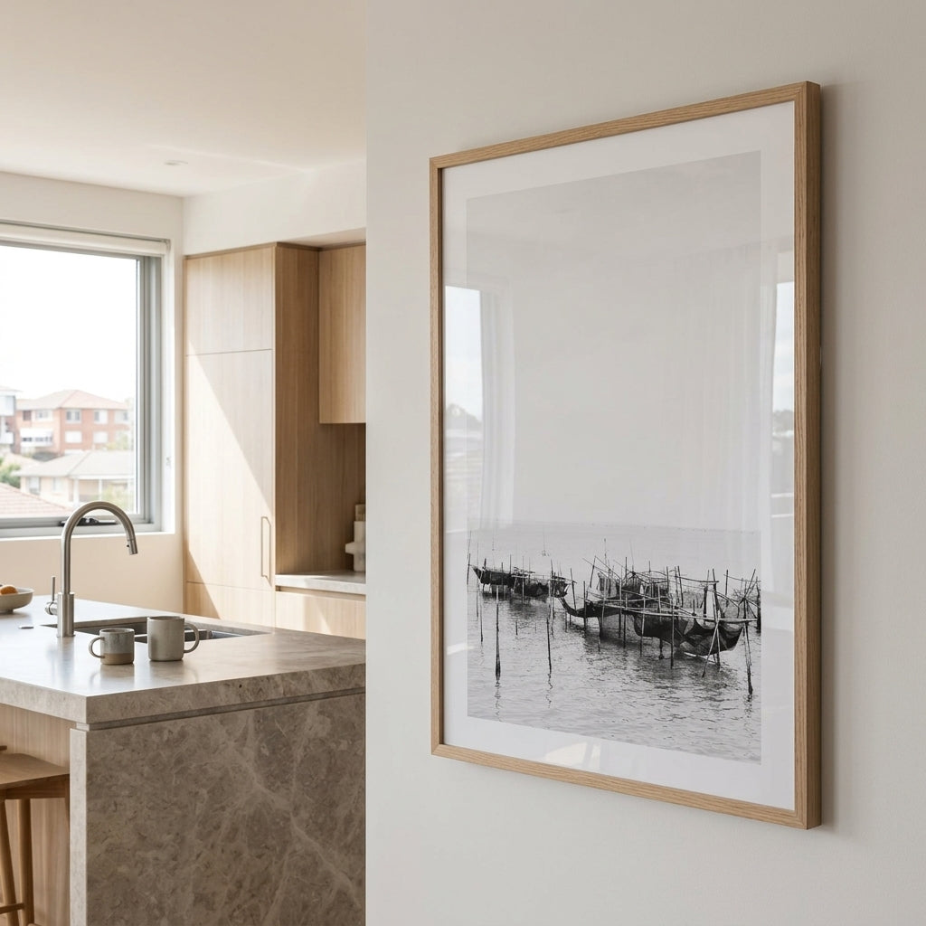 A large framed black and white art print depicting a harbor scene with boats, styled on a light beige wall in a modern kitchen interior.