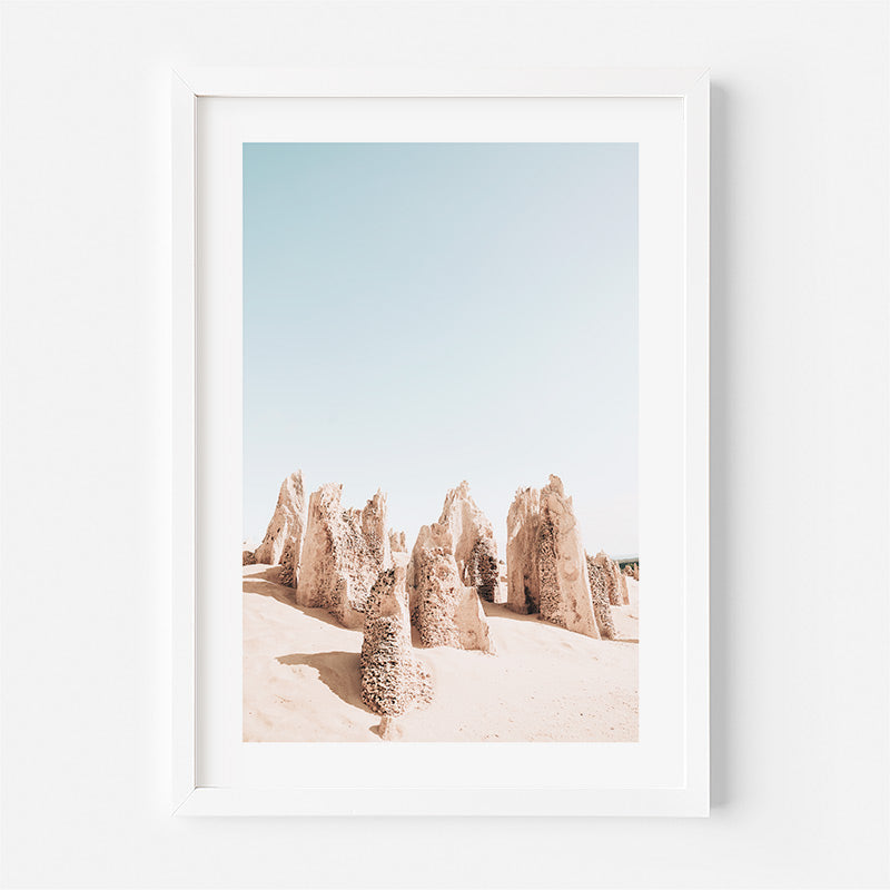 Framed artwork of desert landscape with rock formations against a blue sky.