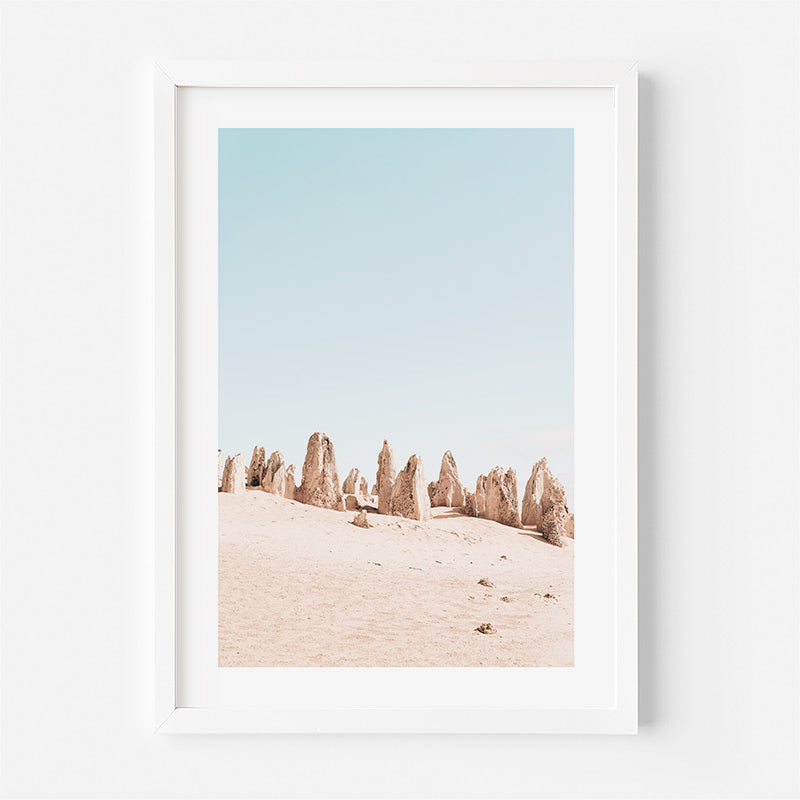 Framed artwork of desert landscape with rock formations against a light blue sky.