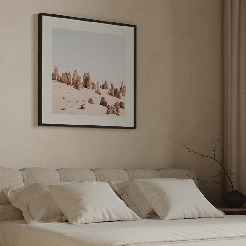Framed landscape print above a bed with neutral tones