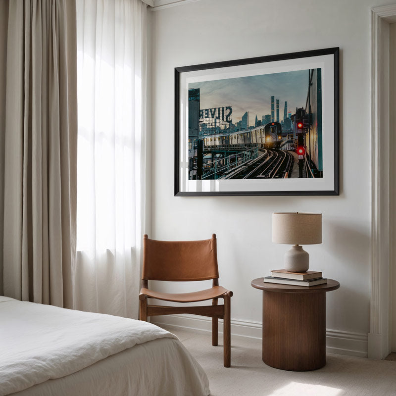 Modern bedroom with a bed, brown chair, side table, and framed artwork on the wall.