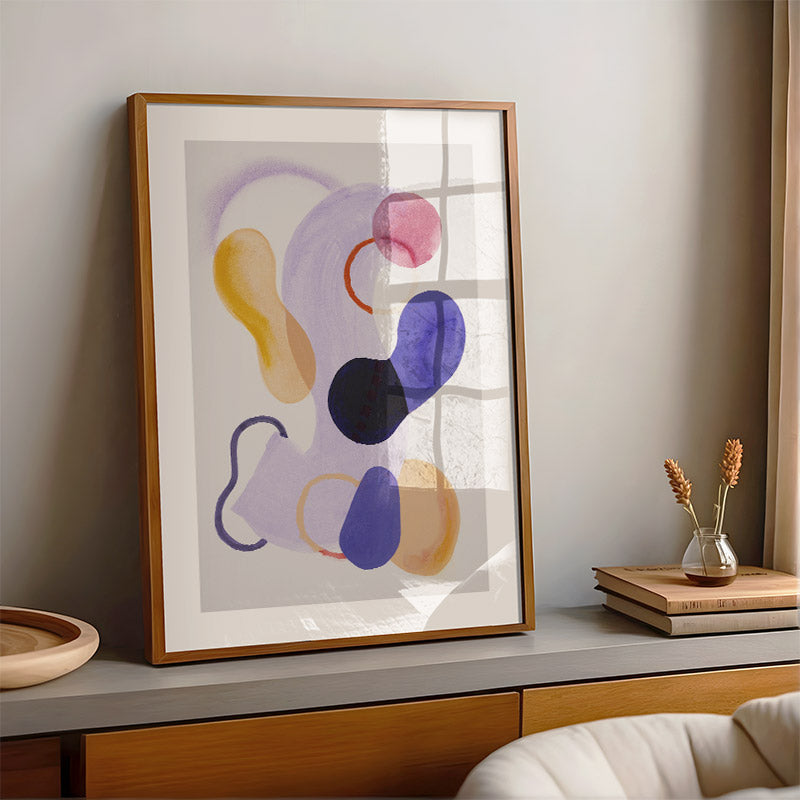 Framed abstract art piece on a shelf with decor items.