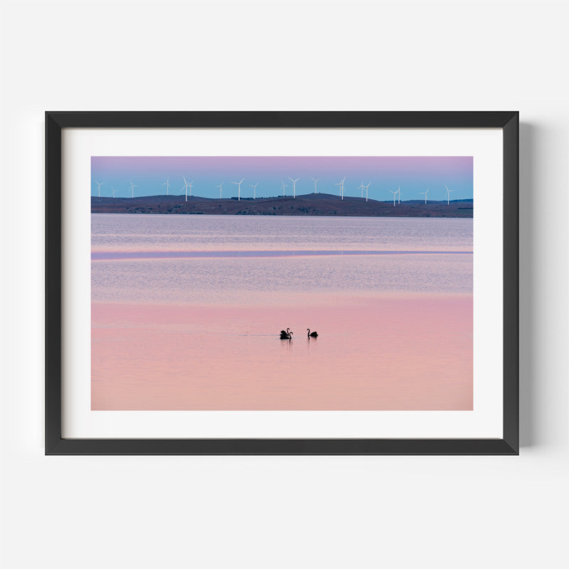 Framed artwork of a landscape with wind turbines and a pink sky.