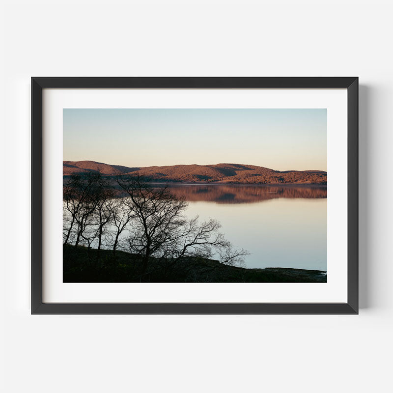 Framed photograph of a landscape with a lake and mountains at sunset.