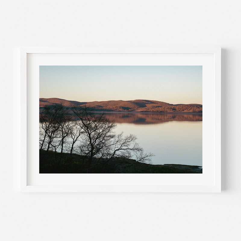Framed photograph of a landscape with a lake and mountains at sunset.