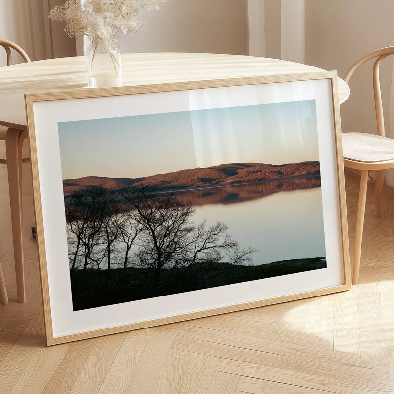 Framed landscape print on a wooden floor with a table and chairs in the background