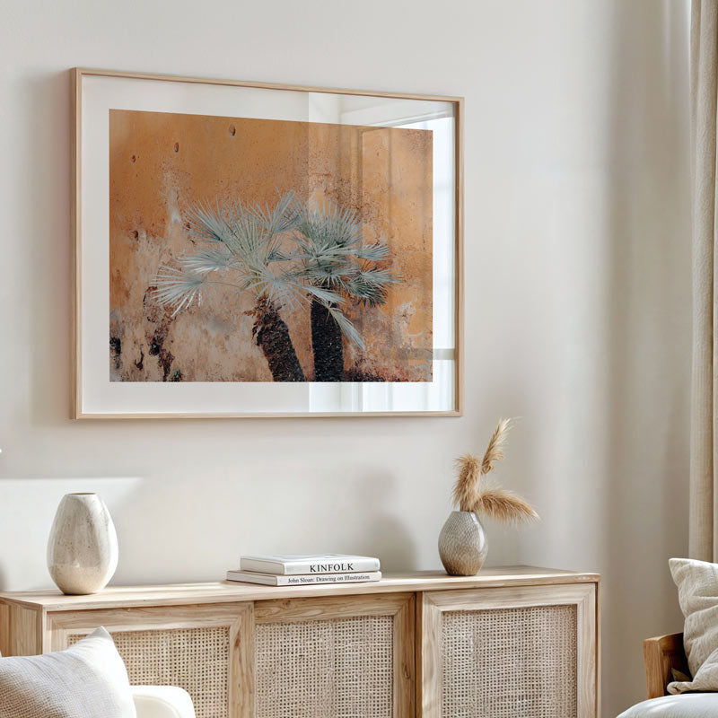 Framed artwork of a palm tree on a wall above a wooden cabinet with decorative items.