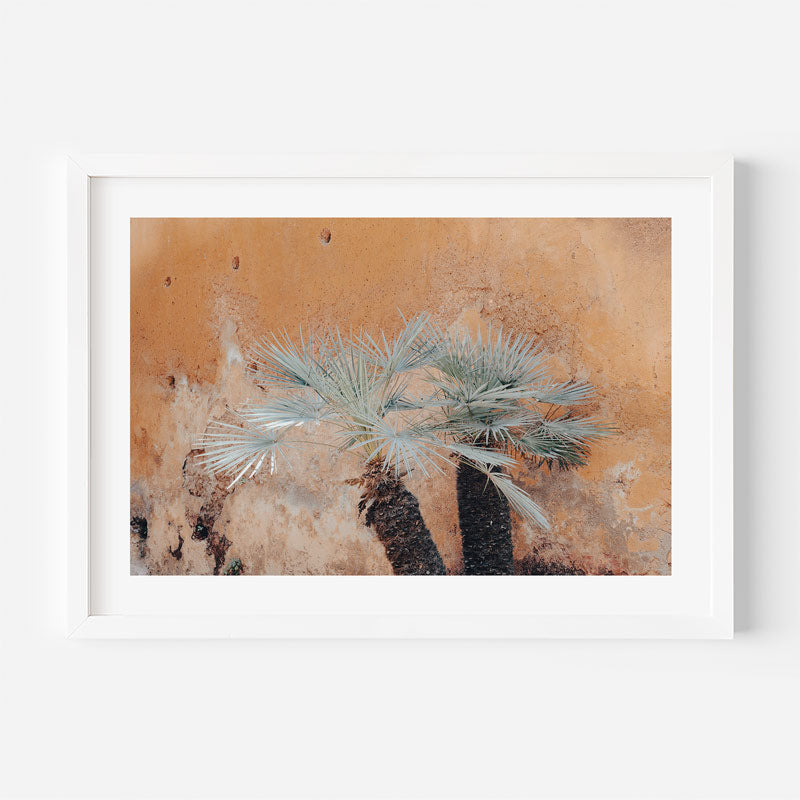 Framed artwork of a palm tree against a textured wall.