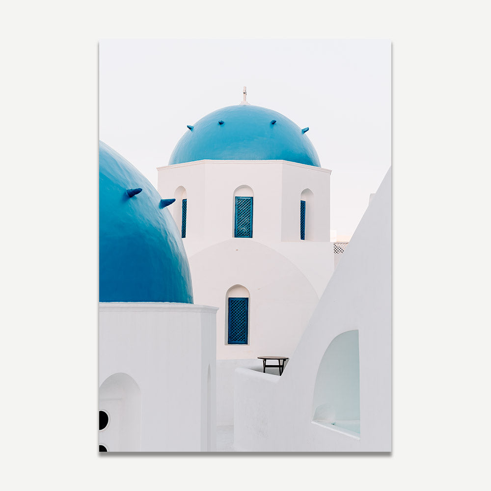 A wall art print featuring whitewashed buildings with blue domes and shutters, characteristic of Mediterranean architecture.