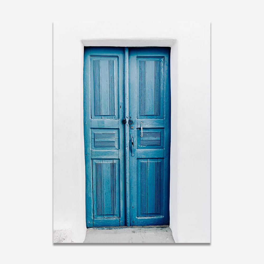 An art print featuring a blue door in Oia, Santorini with white walls and a sun-drenched background.