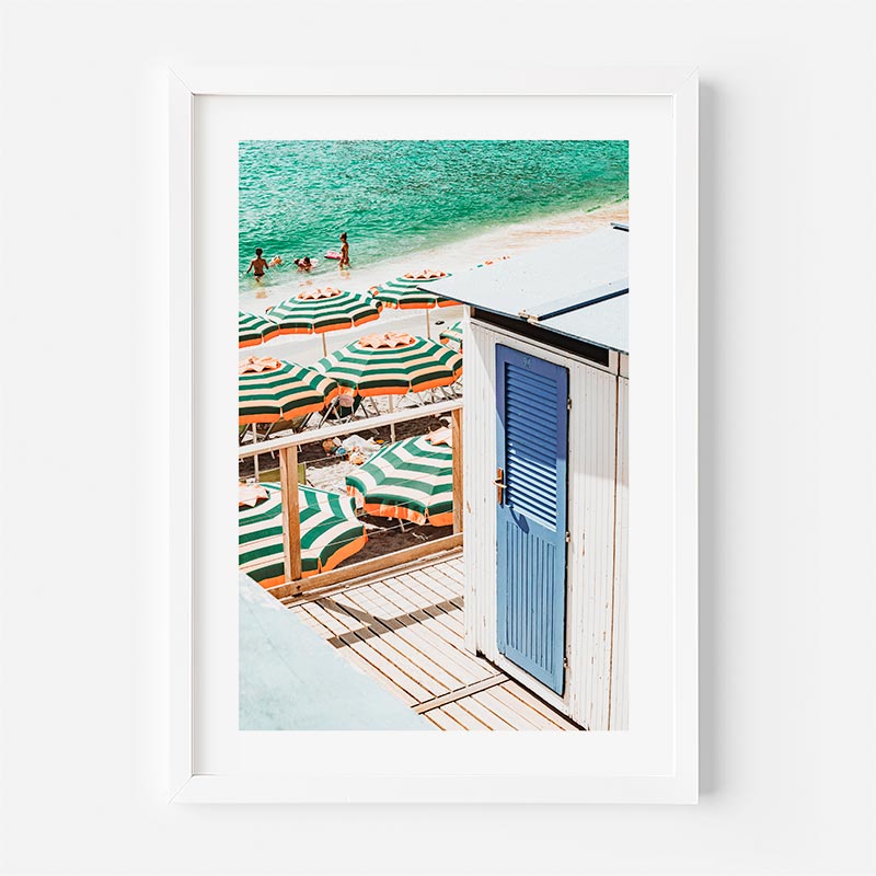 Framed photograph of a beach scene with striped umbrellas and a blue door.