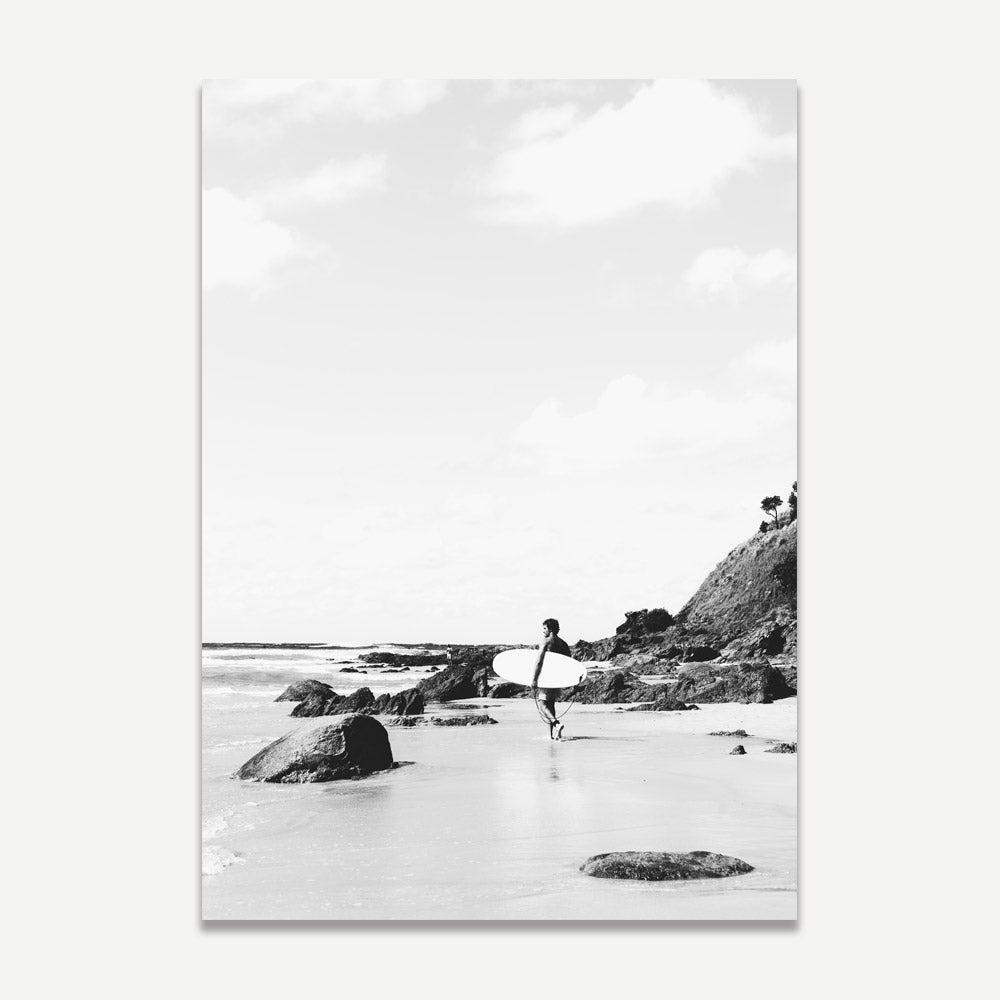 Black and white photograph of a person surfing, with rocks and a cliff in the background, displayed as a print.