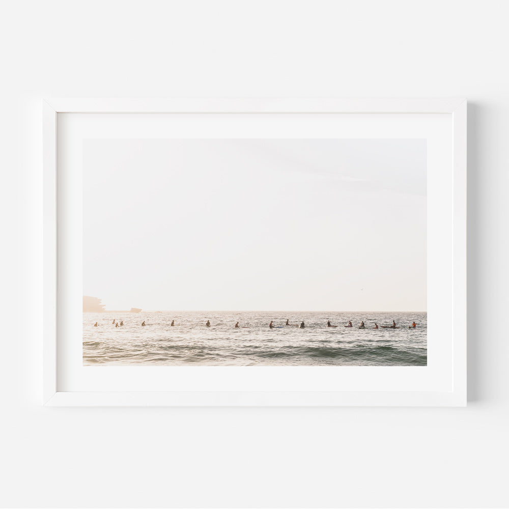 A white framed photo of surfers on the beach, perfect for wall art decor in homes and offices.
