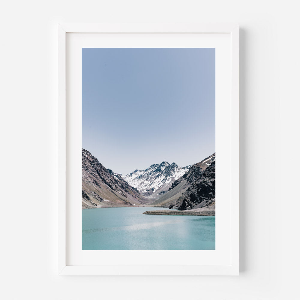 A framed print of a landscape featuring a lake and mountains with a clear blue sky.