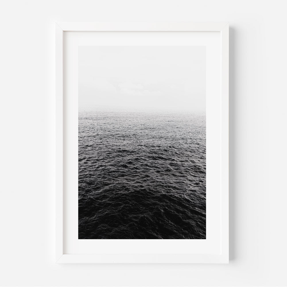 Black and white photograph of a calm ocean horizon, framed and mounted on a wall.