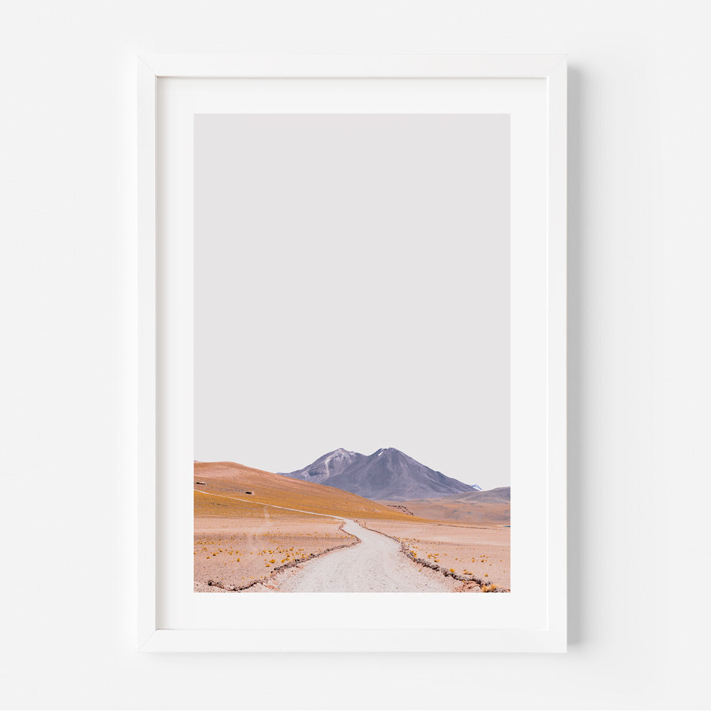 A framed print featuring a landscape with a dirt road leading towards mountains, predominantly in orange and blue colors.