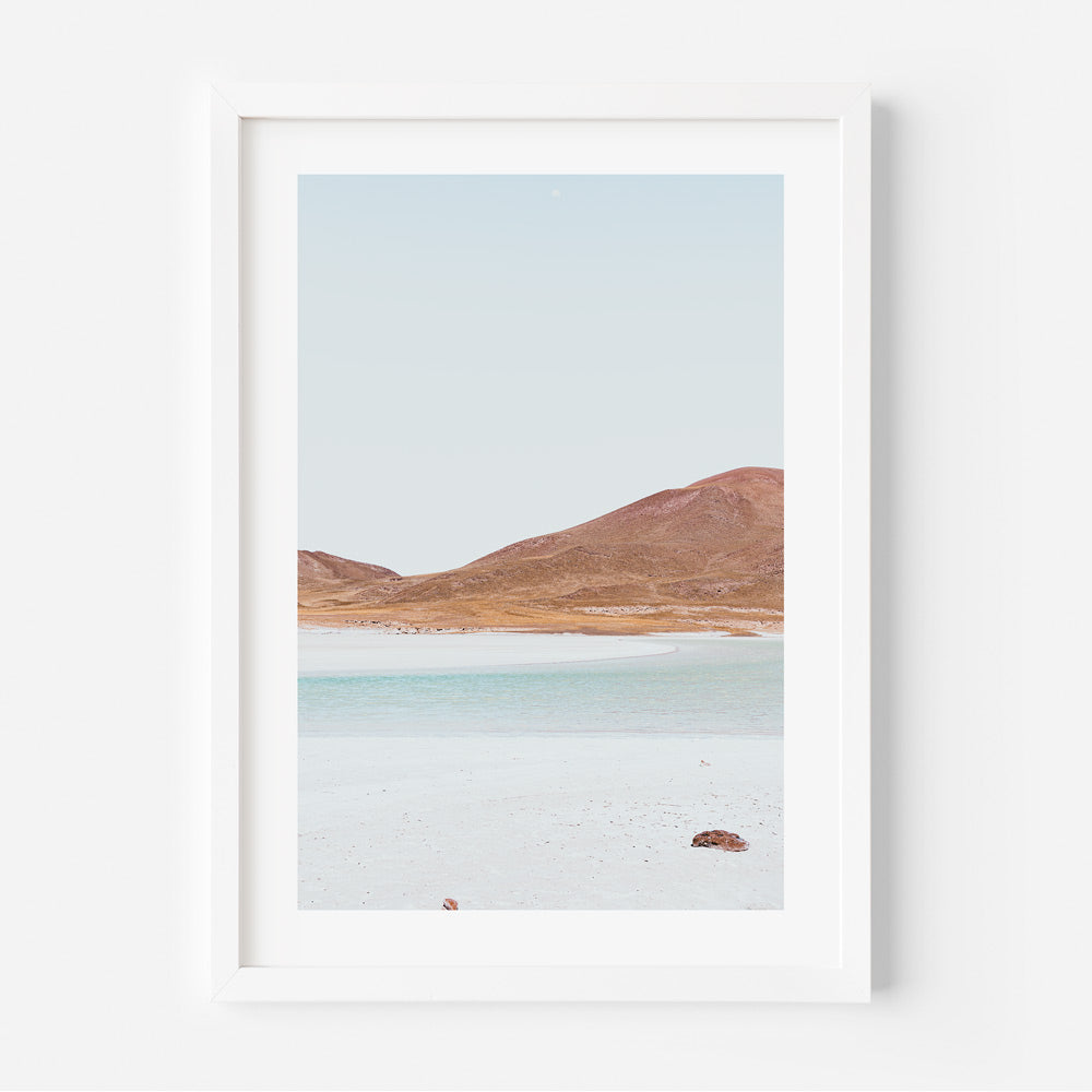 A framed photograph featuring a landscape with blue sky, orange hills, and a body of water, likely representing a scene from Atacama, Chile.