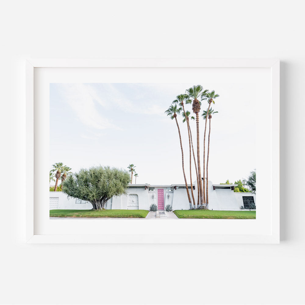 A framed photograph of a house with a pink door, surrounded by palm trees, in Palm Springs.