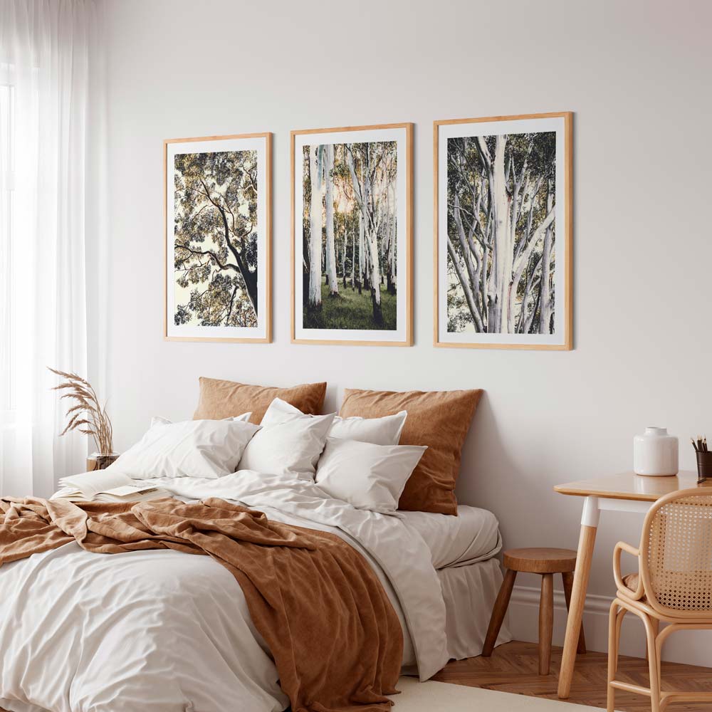 A set of three framed artwork pieces hanging above a bed in a bedroom setting