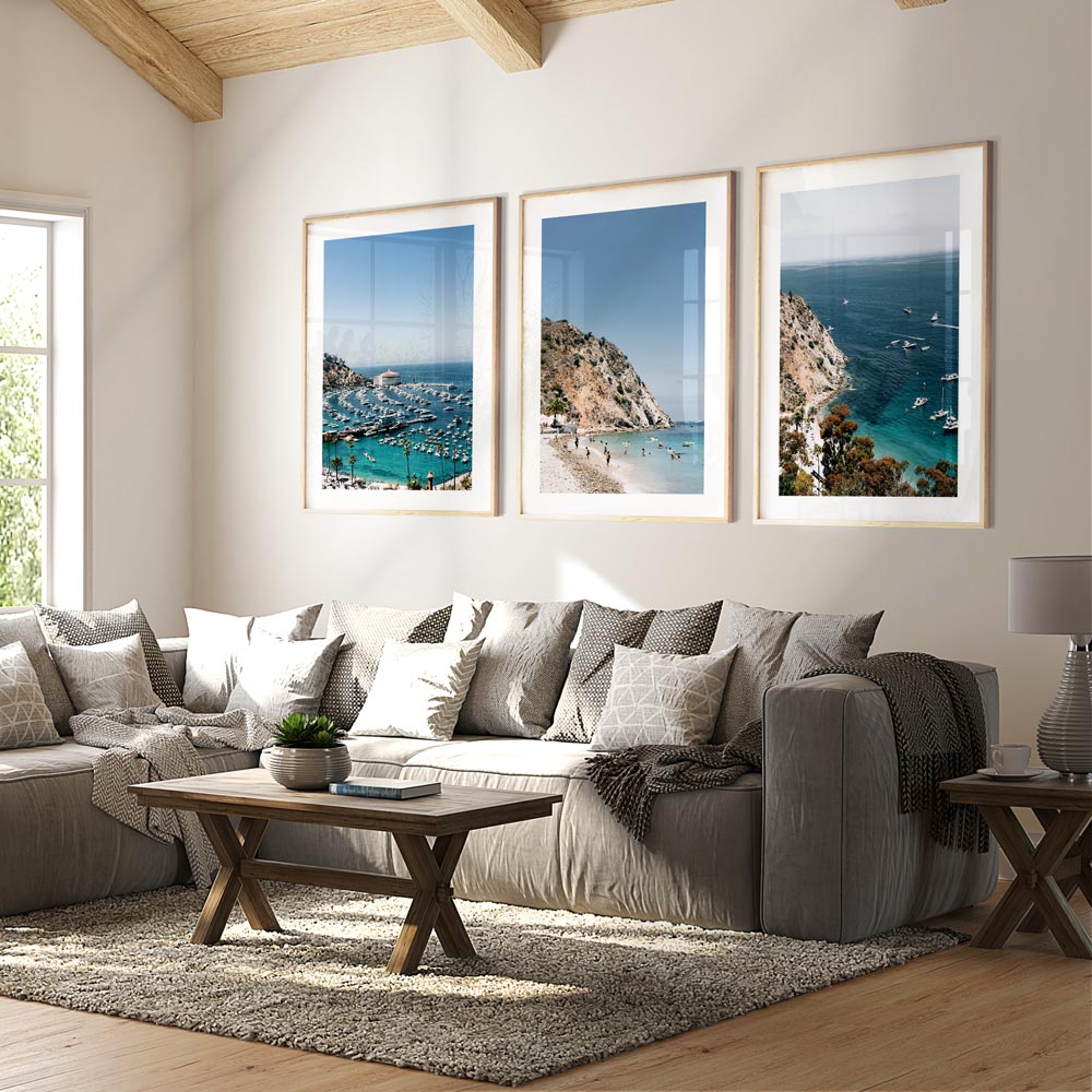 A set of three framed wall art depicting a beach scene, hanging on a wall above a grey sofa in a living room setting.