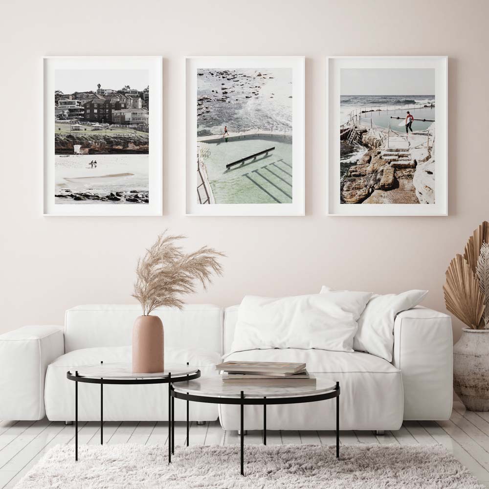 A set of three framed photographs on a wall above a white sofa, with content featuring coastal landscapes and a pool.