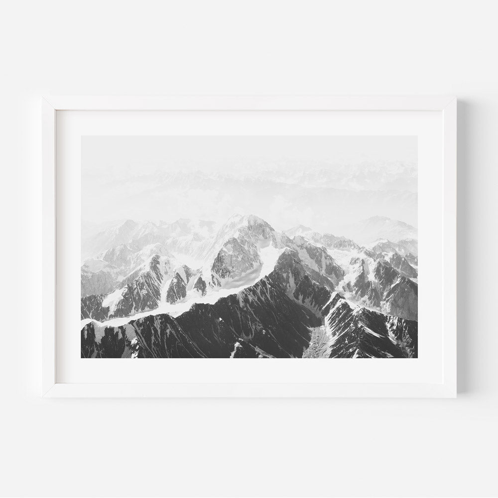 A black and white photograph of snowcapped mountains with a white border, presented in a simple black frame.