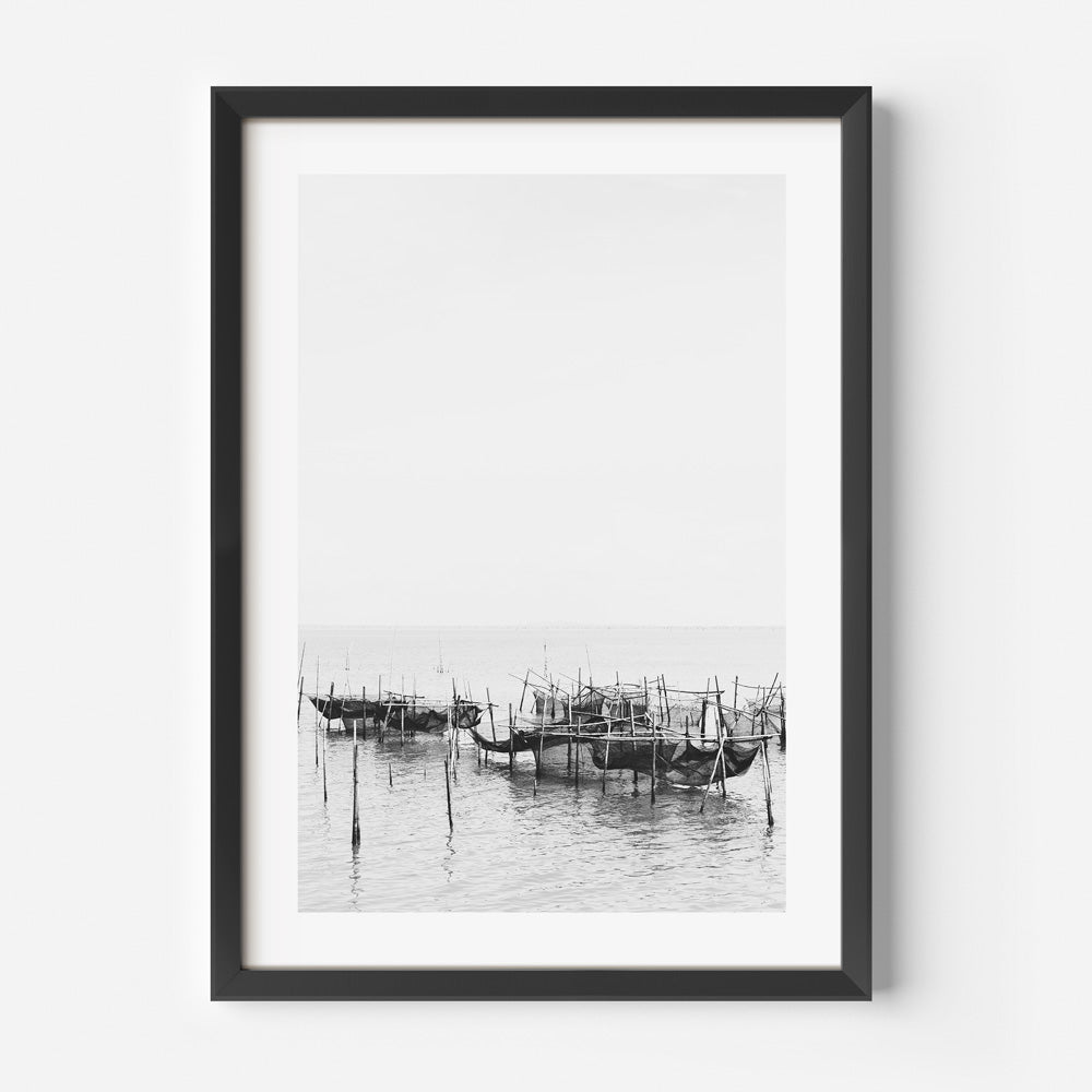 Black and white photograph of a fishing village with boats and wooden structures, captured within a black frame.