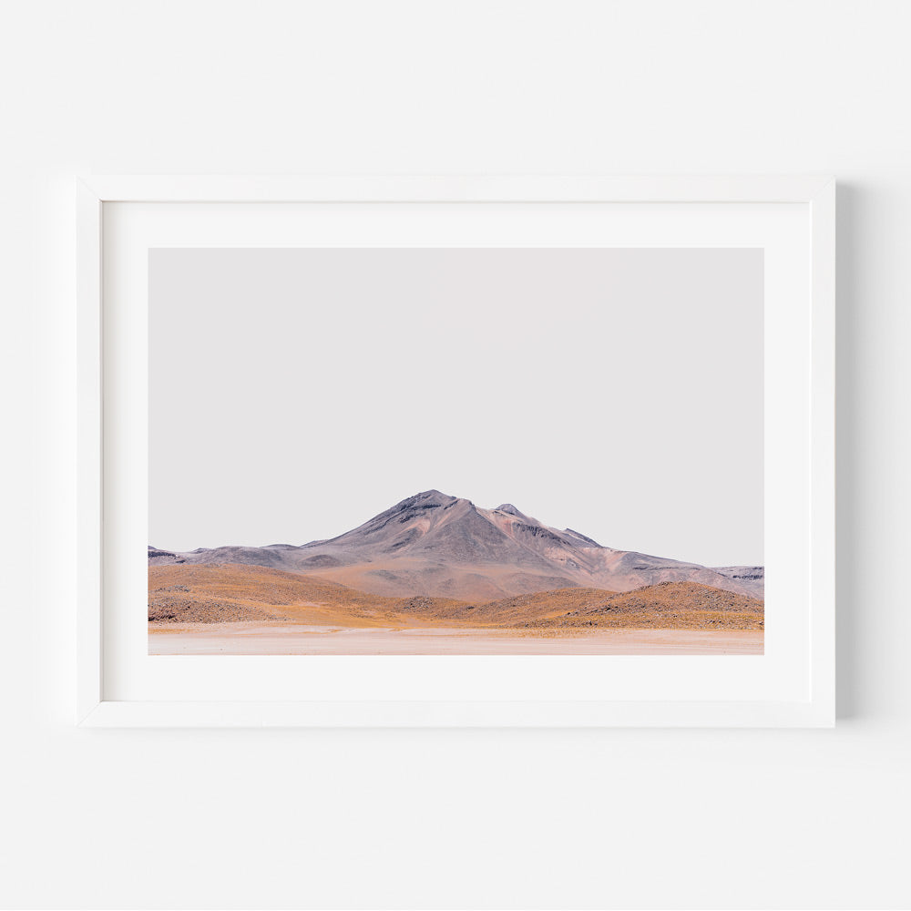A framed photograph of a landscape featuring a mountain range with orange and purple hues against a white background.