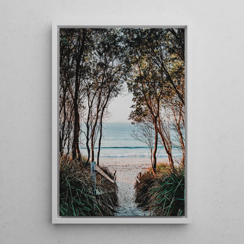 Framed artwork of a beach scene with trees and ocean view on a white wall.