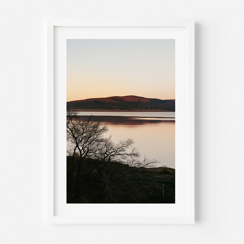 Framed photograph of a sunset over a lake with mountains in the background.
