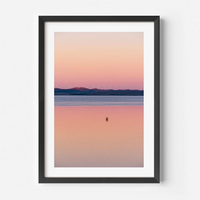 Framed artwork of a sunset over water with mountains in the background
