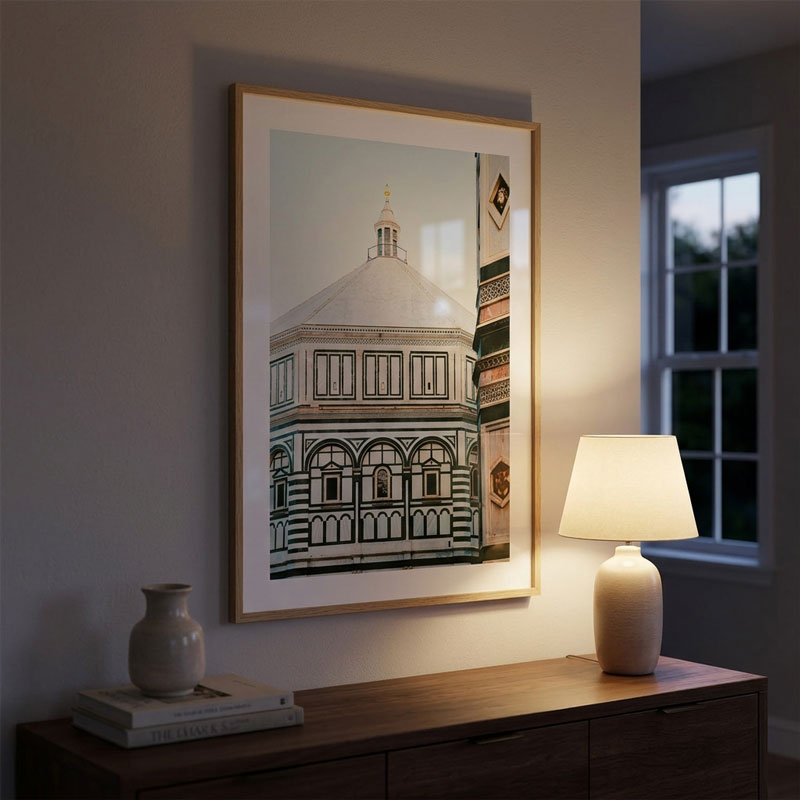 A framed art print of the Florence Cathedral dome hangs on a warm-toned wall above a wooden console table with a lit table lamp and a small vase.