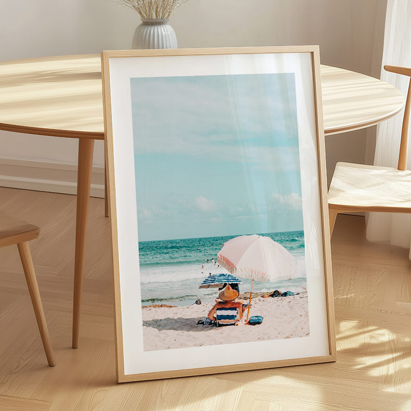 Framed photograph of a beach scene with a person and umbrella on a wooden table.
