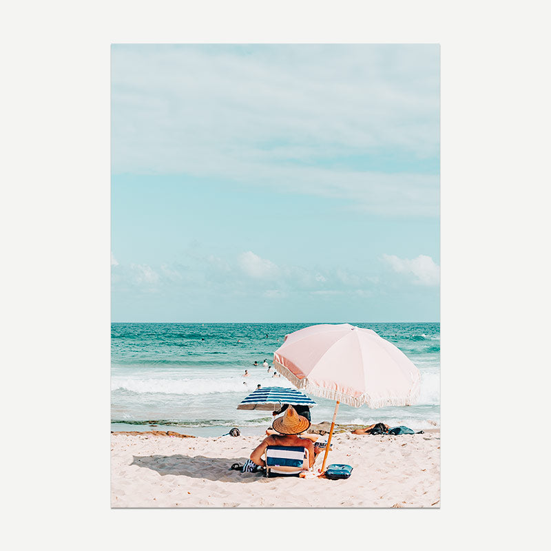 Person with a pink umbrella on a beach with clear blue sky and ocean.