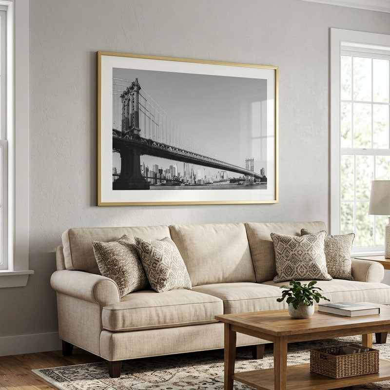 A large framed black and white photograph of the Brooklyn Bridge hanging on a light gray wall above a beige sofa in a styled living room.