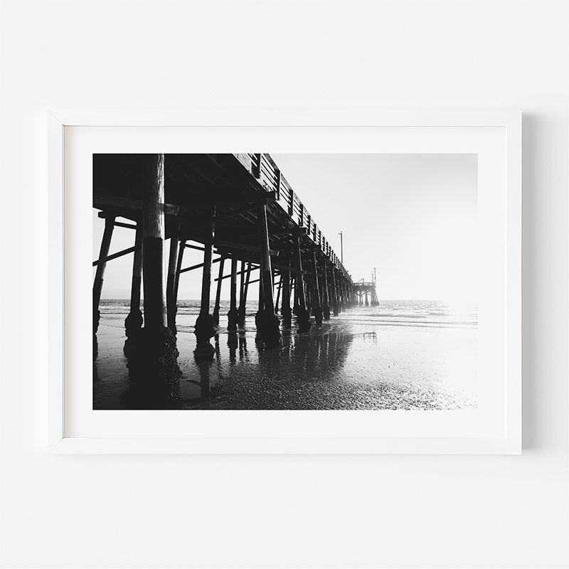Black and white photo of a pier on a beach