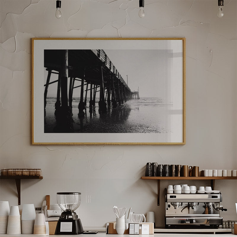 Framed black and white photo of a pier on a wall above a coffee shop counter.
