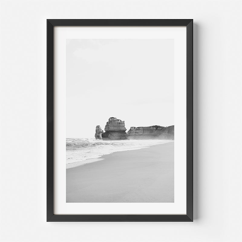 Framed black and white beach print with rock formations on a white wall
