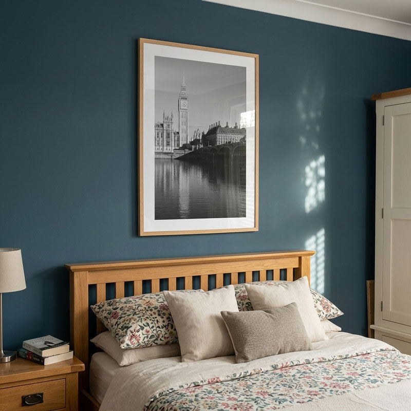 A framed black and white photograph of Big Ben and London landmarks hangs on a dark blue wall above a wooden bed with floral-patterned bedding in a styled bedroom.