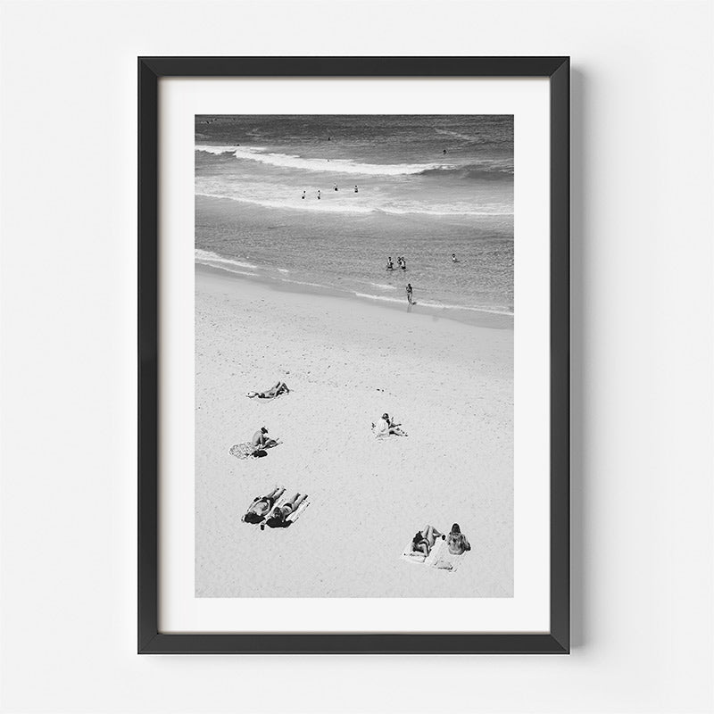 Framed black and white beach scene with people and footprints.