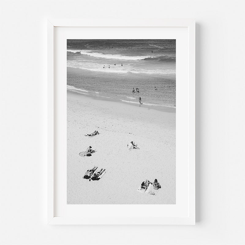 Framed black and white beach scene with people and dogs on a sandy shore.