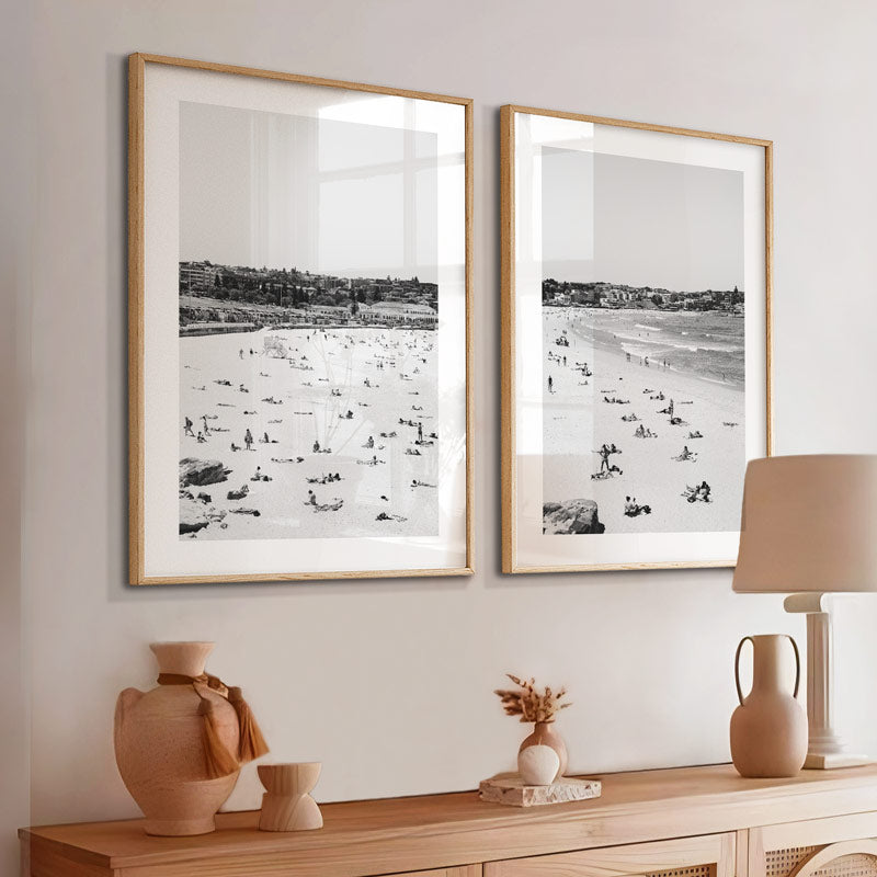 Two framed black and white beach scenes on a wall above a wooden console table with decorative items.