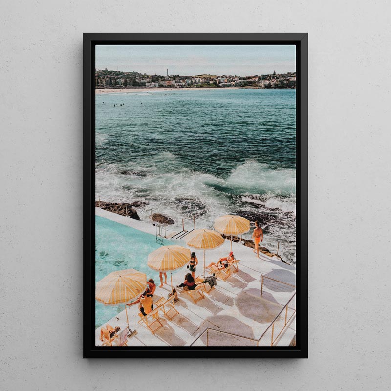 Framed photograph of a poolside scene with people under yellow umbrellas by the ocean.