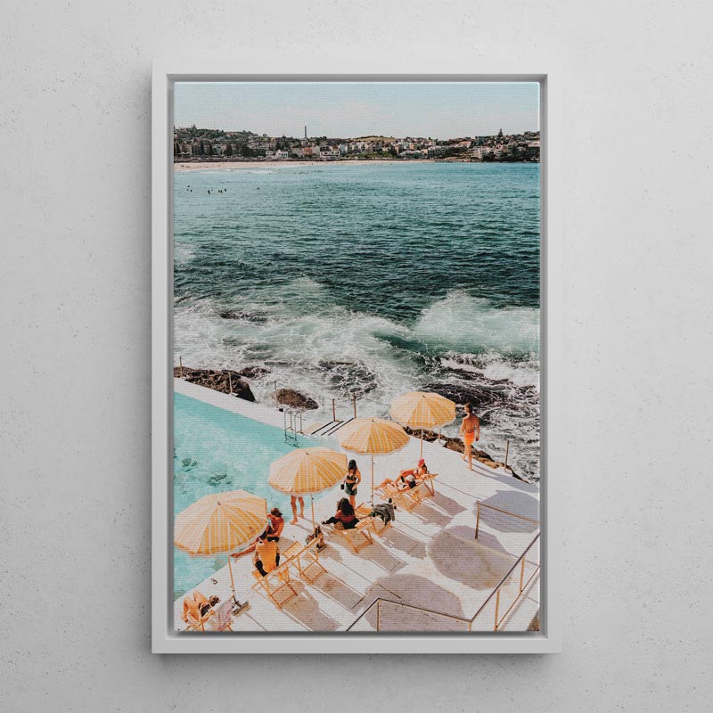 Framed artwork of a poolside scene with people under yellow umbrellas by the ocean.