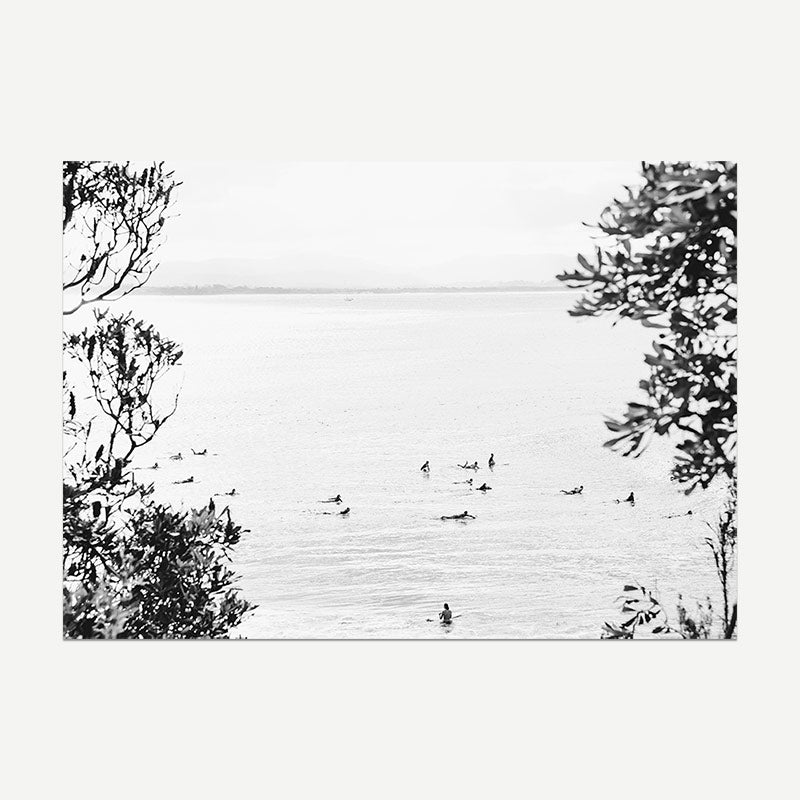 Black and white photography of surfers on the water with trees framing the scene