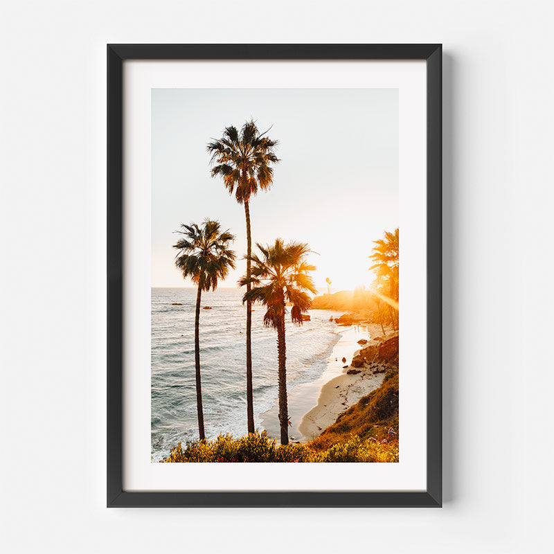 Framed artwork of a beach scene with palm trees and sunset.