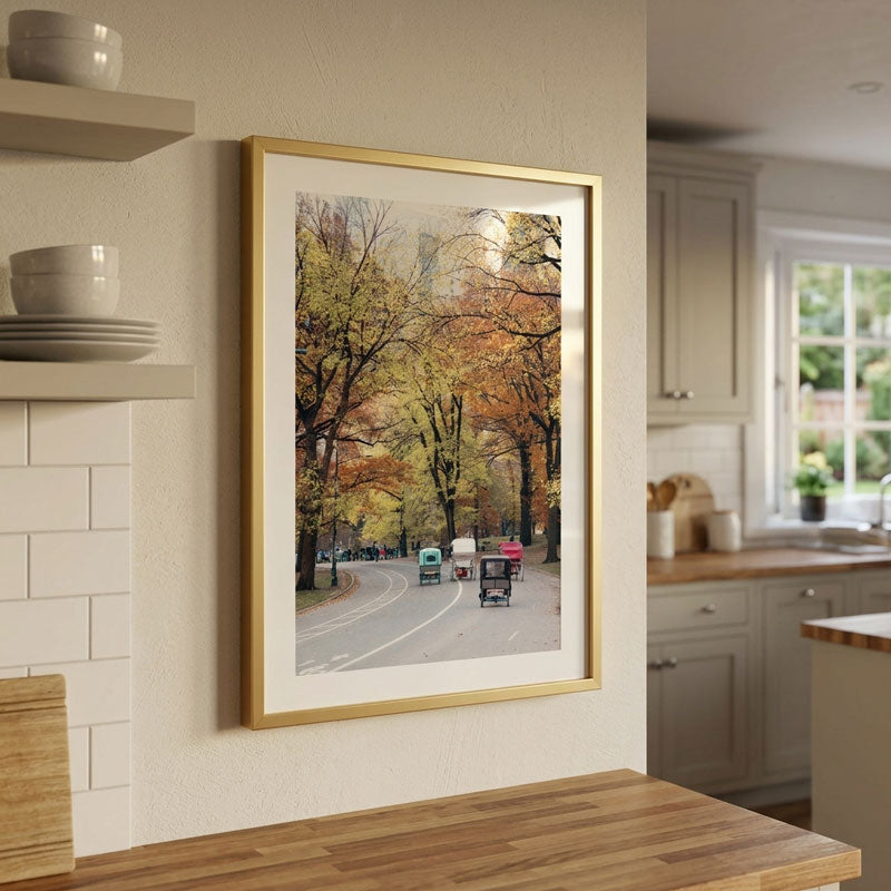 A framed art print depicting an autumn street scene with colorful cars and trees, displayed on a beige wall in a modern kitchen setting.