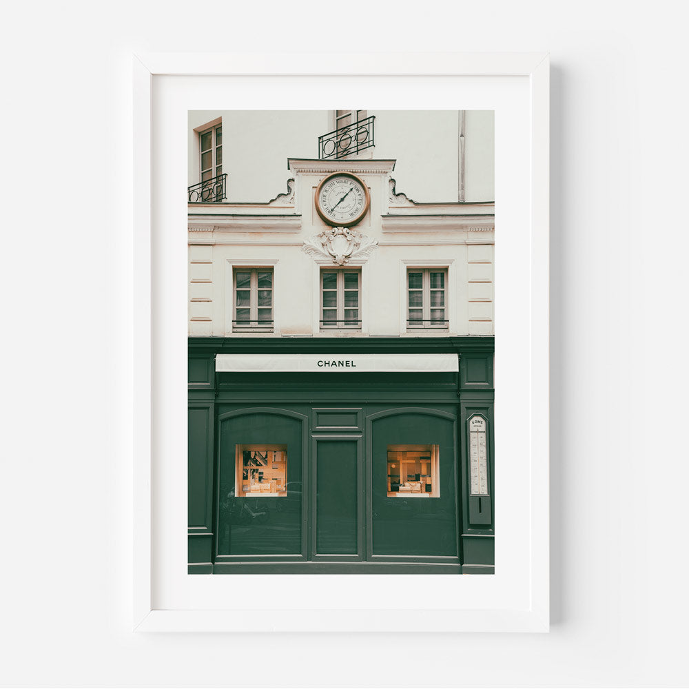 A green and white framed photo of a building with a clock, showcasing the iconic Chanel building in Paris, France.