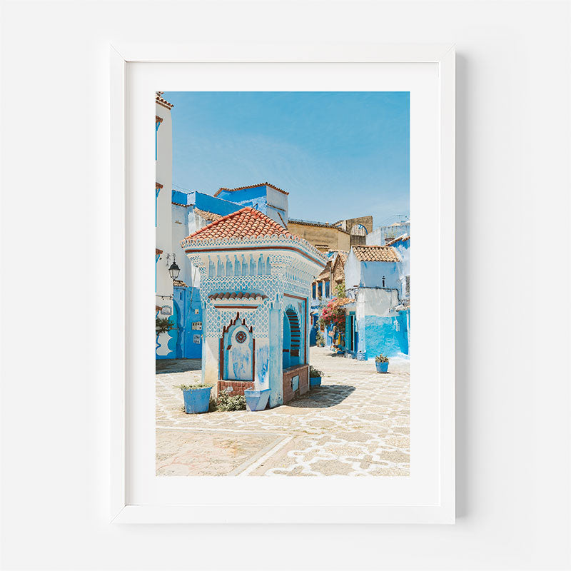 Framed photograph of a picturesque street with blue buildings and a white frame.