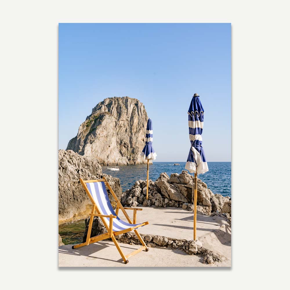 La Fontelina Beach Club in Capri, featuring blue and white beach umbrellas and sun decks on rocky shores with the shimmering Mediterranean Sea and Capri Island in the backdrop, captured during the serene late afternoon.